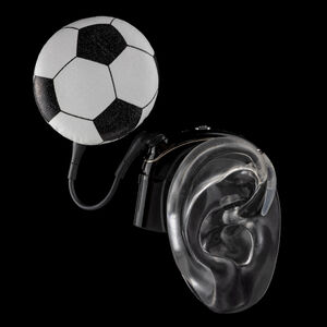 Black ear mould shows cochlear implant with coil hat in a football design